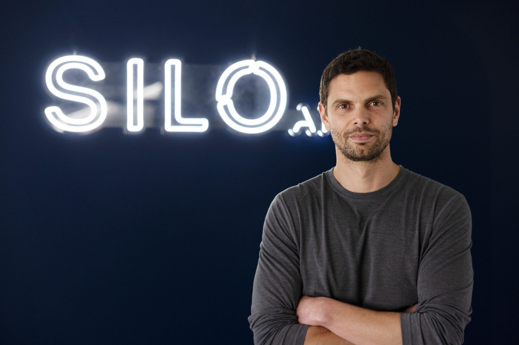 A man stands in front of a neon sign that reads "Silo AI".